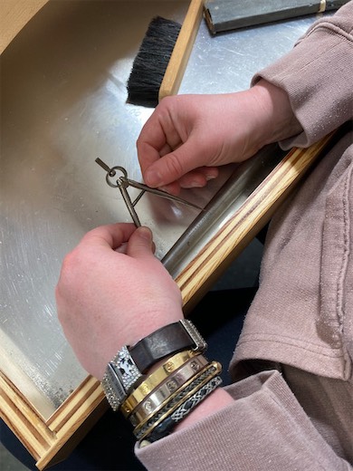 Hands filing a small jewelry piece at a bench pin